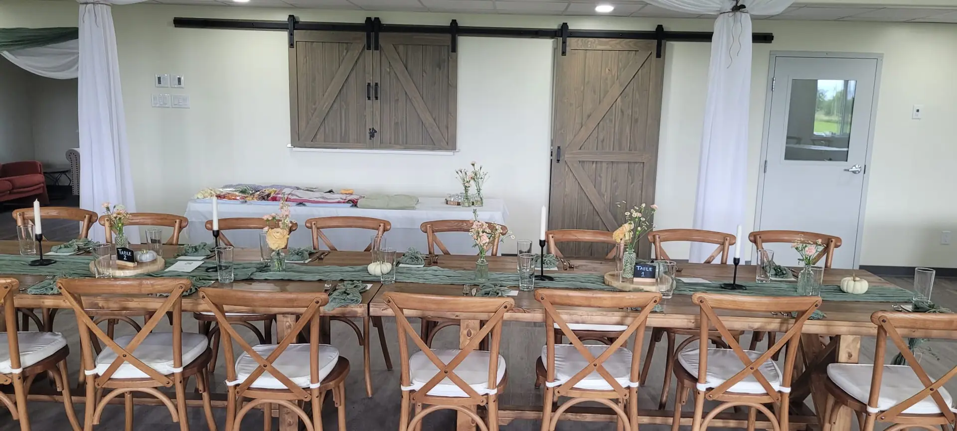 A sheer backdrop with greenery and warm bulbs behind a table, brought in by the party who booked the hall