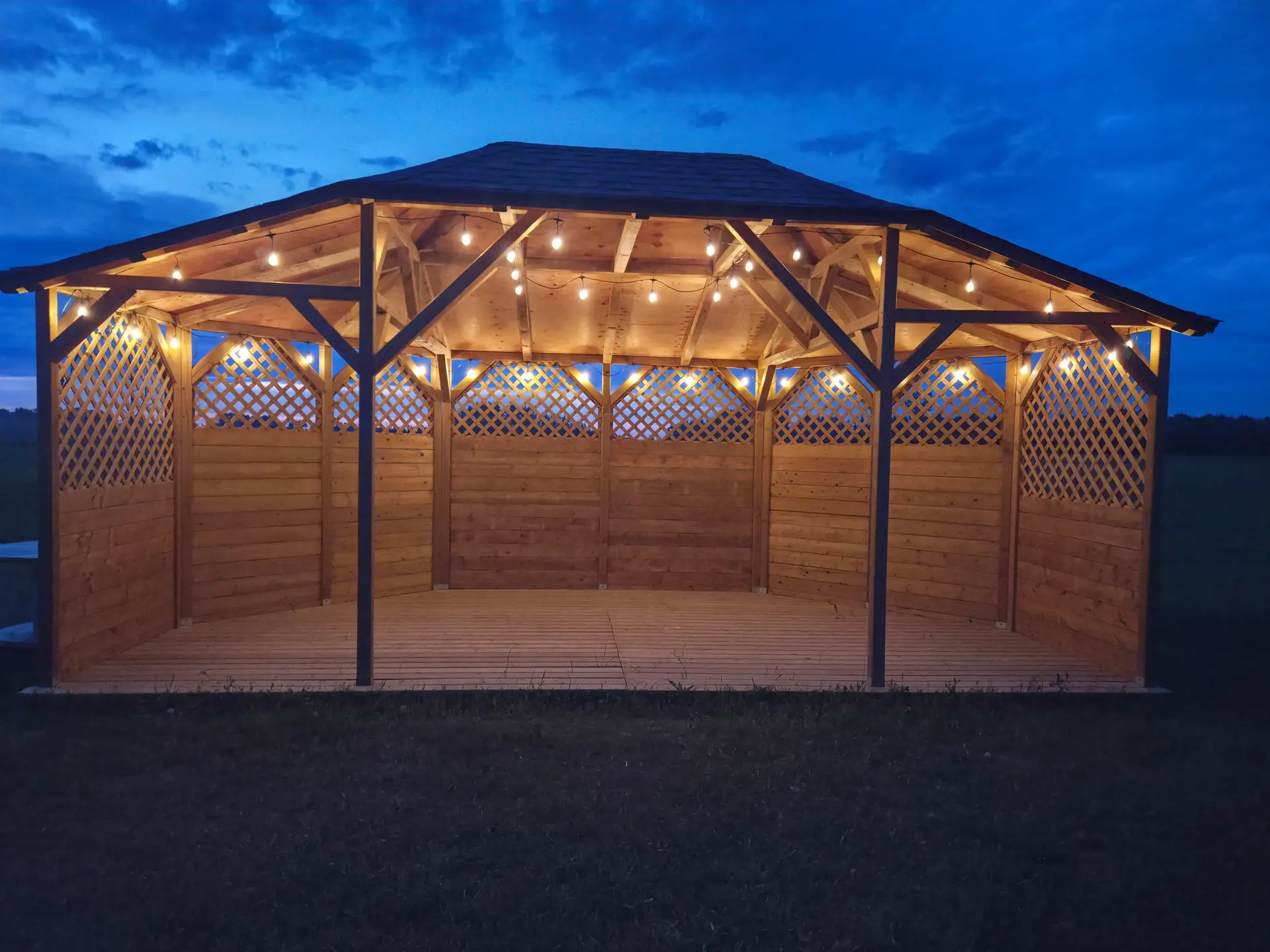 The gazebo at Bristol Event Centre lit with warm bulbs at dusk, with the field behind it